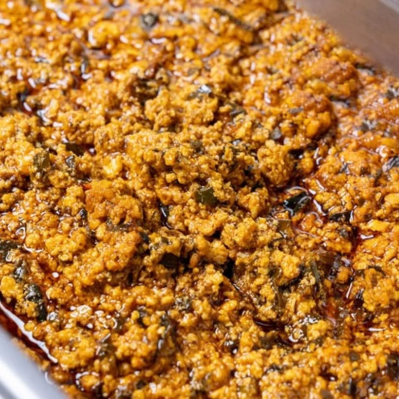 Close-up of a Nigerian dish with a textured, golden-brown base and dark green specks.