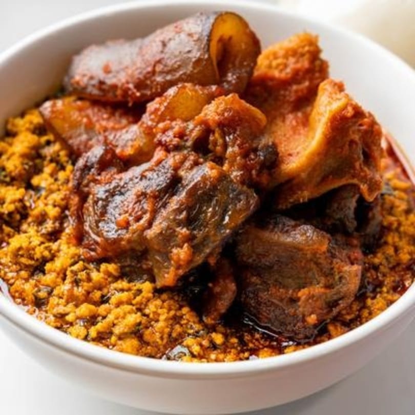A white bowl filled with Nigerian gbegiri soup and ewedu, topped with assorted meats.