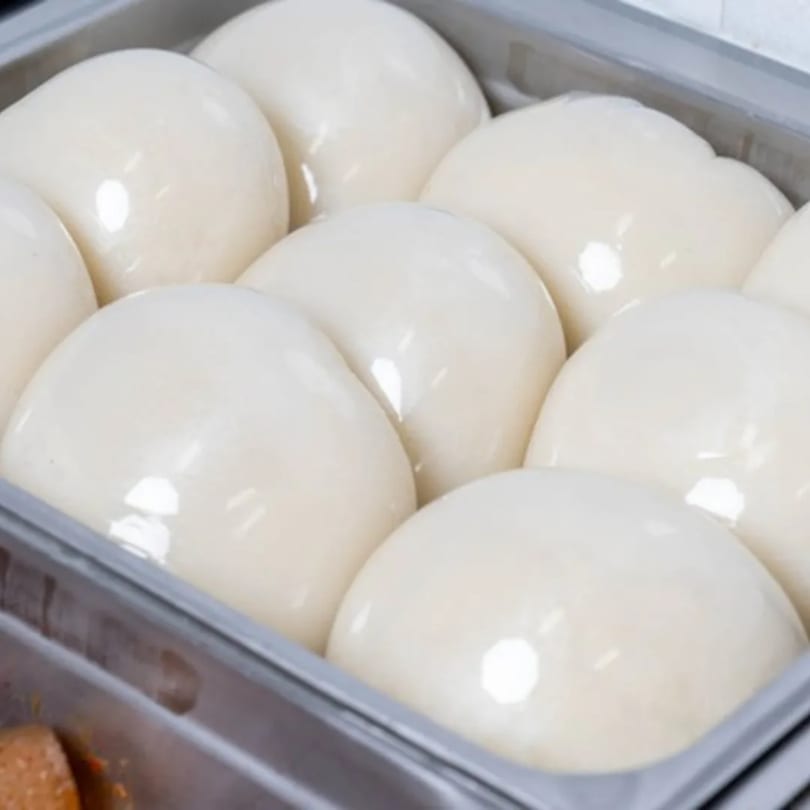 Several smooth, white, dome-shaped Nigerian fufu portions are neatly arranged in a metal serving tray.