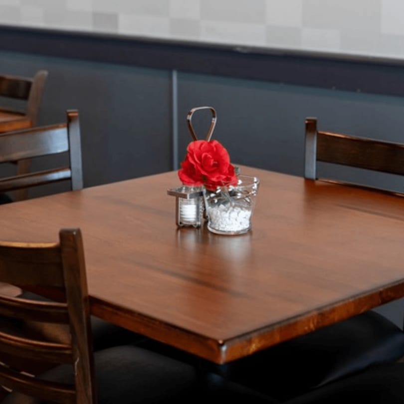 A wooden dining table with a red flower centerpiece, salt, and pepper shakers.