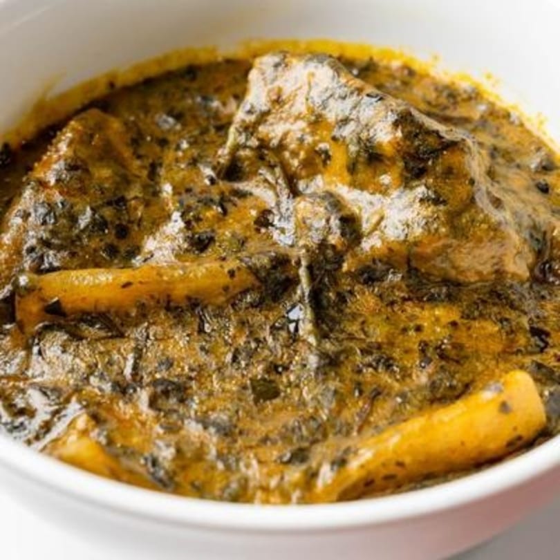 Close-up of a Nigerian dish with dark green and yellow stew, featuring pieces of meat.