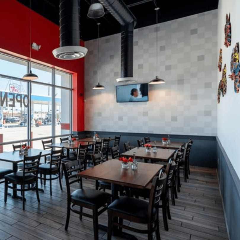 Interior of Rodo Nigerian Cuisine with dining tables, chairs, red accent wall, and large windows.