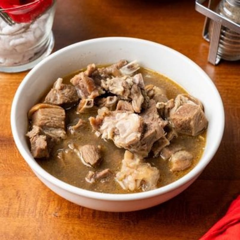 A white bowl filled with Nigerian goat meat pepper soup, featuring tender meat pieces in a rich broth.