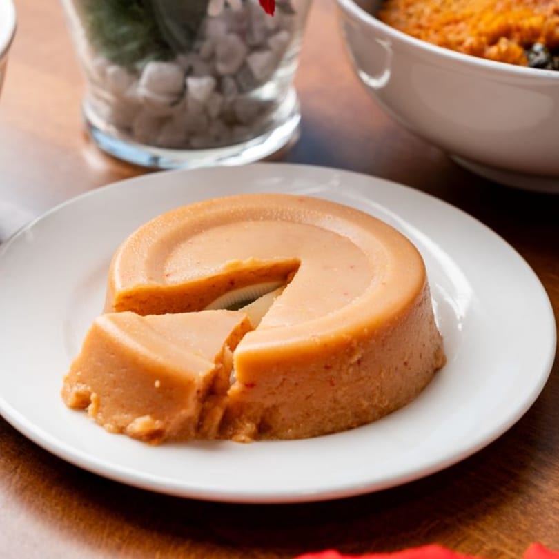 A round, light brown Nigerian moi-moi with a slice cut out, on a white plate.