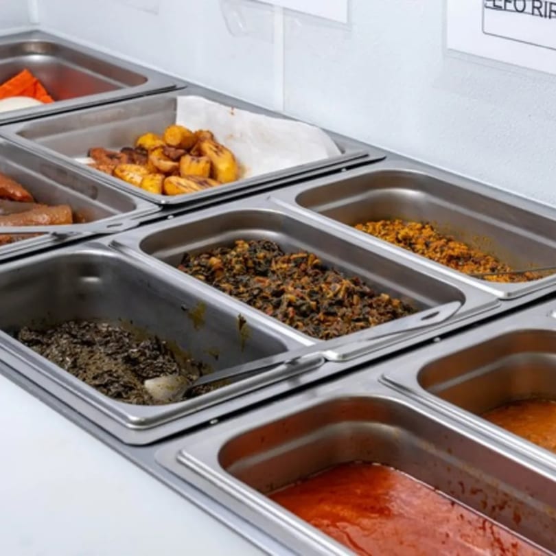 A buffet line at Rodo Nigerian Cuisine with various dishes in stainless steel trays, including plantains and stews.