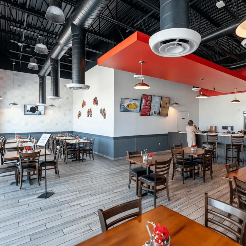 Spacious Rodo Nigerian Cuisine dining room with wooden tables, chairs, and a red accent ceiling.